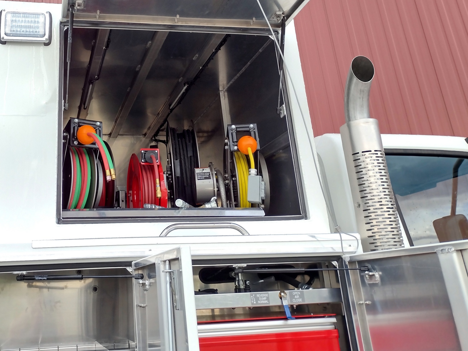 View from right side of a truck into an aluminum service body superstructure compartment with electric, acetylene, and air hose reels.