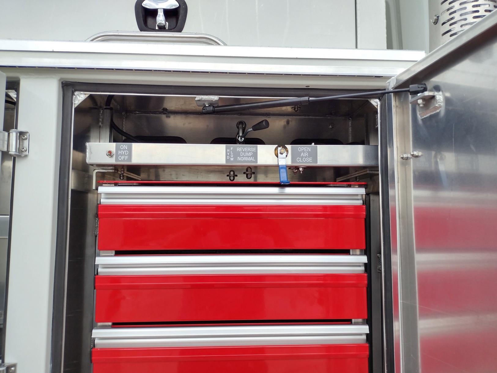 View from right side of a truck into an aluminum service body compartment with electric, acetylene, and air hose reel controls