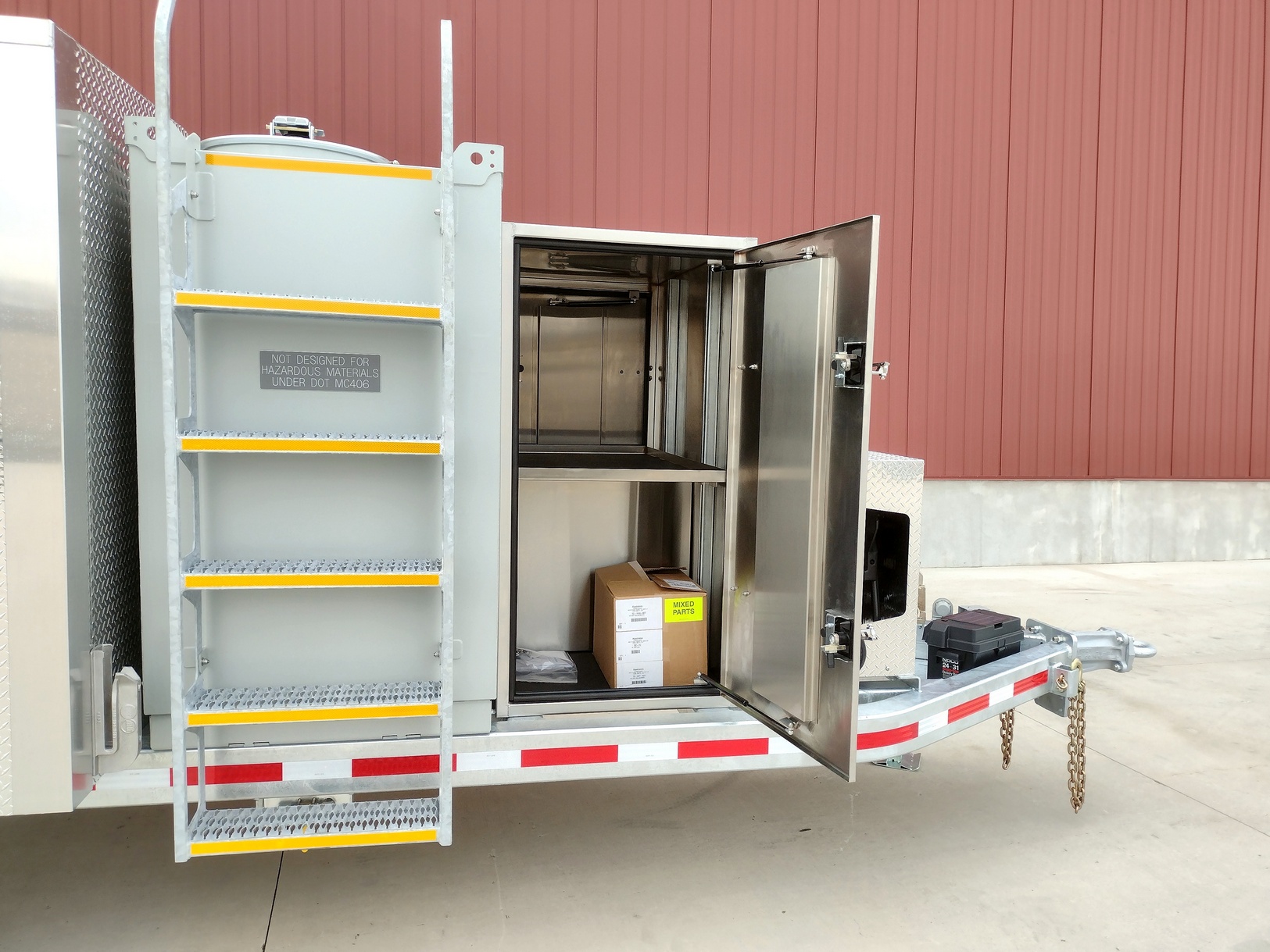 Right side view of the front of a Sauber Model 1594 Oil Filtration Trailer showing the stainless-steel tank and stainless-steel lockable storage Box on concrete with red building in the background
