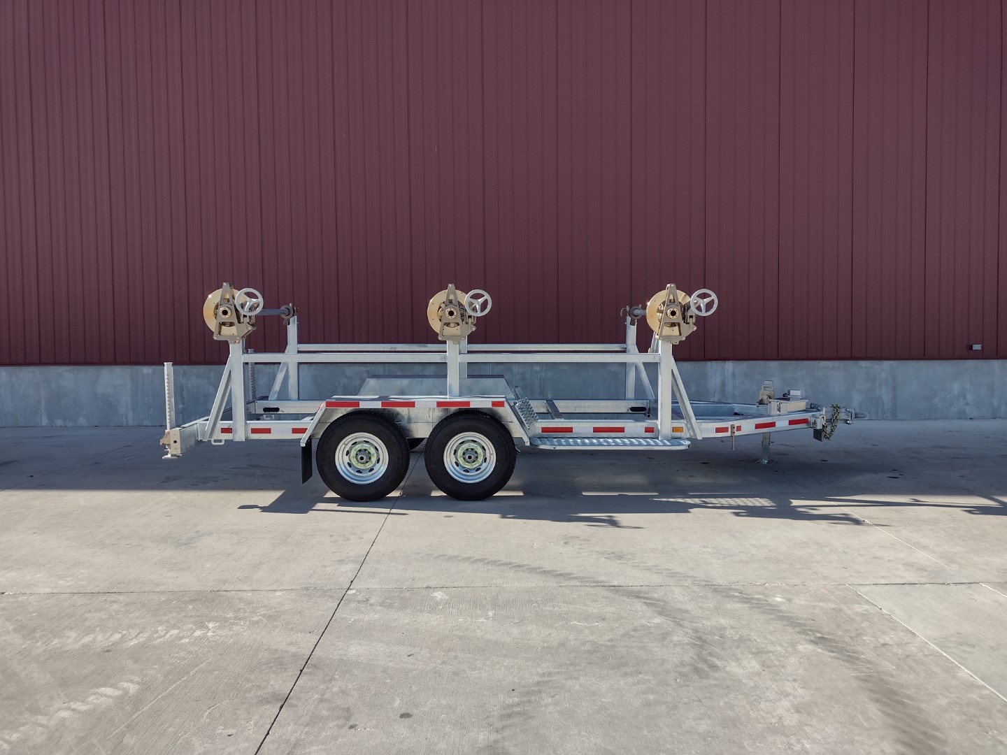 Right side view of Model 1530 Three Reel Trailer with Model 1602 All Bronze Tensioning Brakes shown in front of a red metal building on concrete.