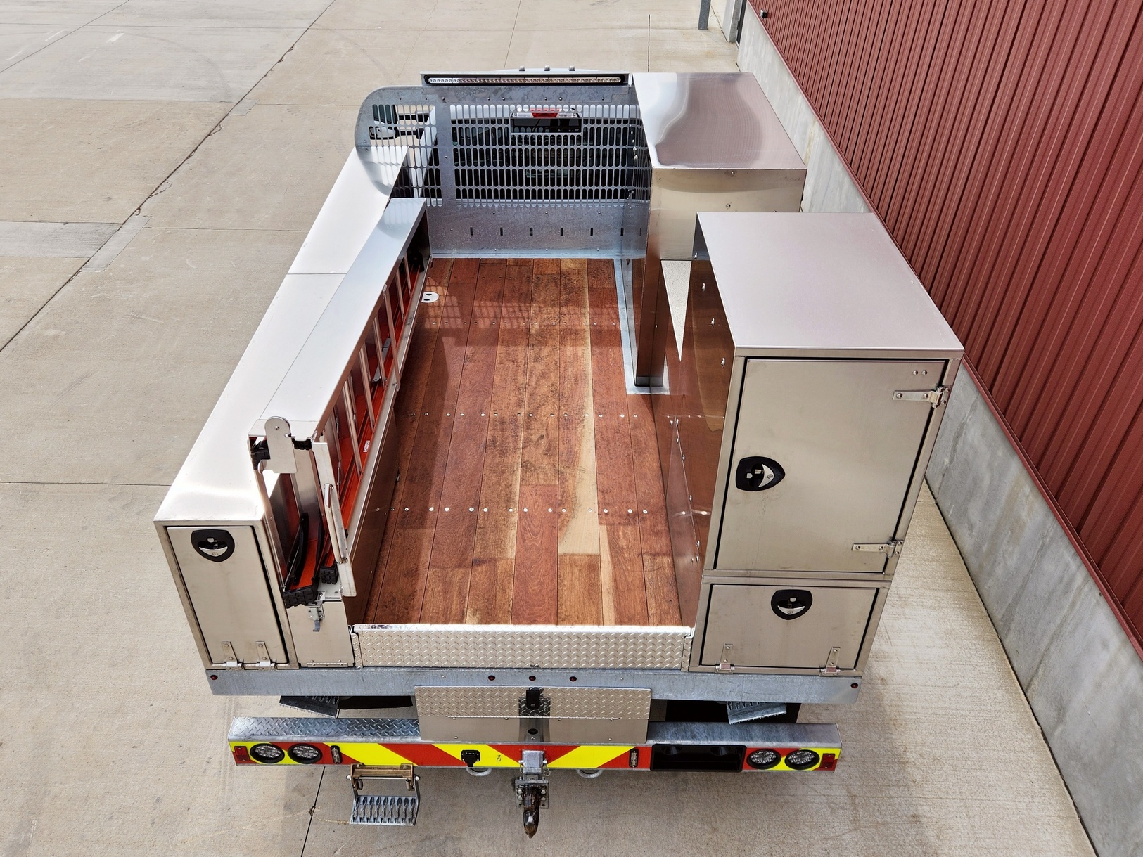 View from rear and above of a Sauber Mfg. Co. Sign Truck Galvanized Platform Crane Body with Galvanized Bulkhead, Angelim Flooring, Stainless Steel Toolboxes and Step Ladder Storage. Boxes. Custom designs provide storage for sign maintenance tools and materials that you need. The truck is shown on concrete.