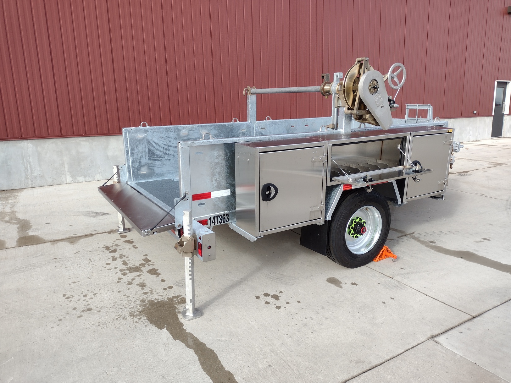 Right side view from rear of a Sauber Model 1560 Reel Cargo Trailer with galvanized finish on concrete in front of a red metal building.