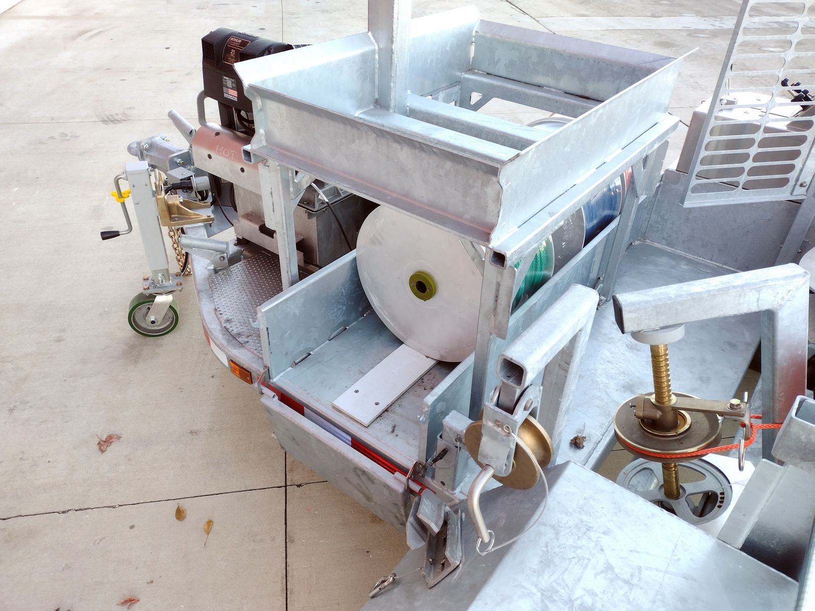 Tight Left side view of the rope storage area below the payout bracket stand of a 1570-B Puller. The trailer is shown on a concrete pad. Also visible are parts of the pulling table, jack, power source and solar battery box.