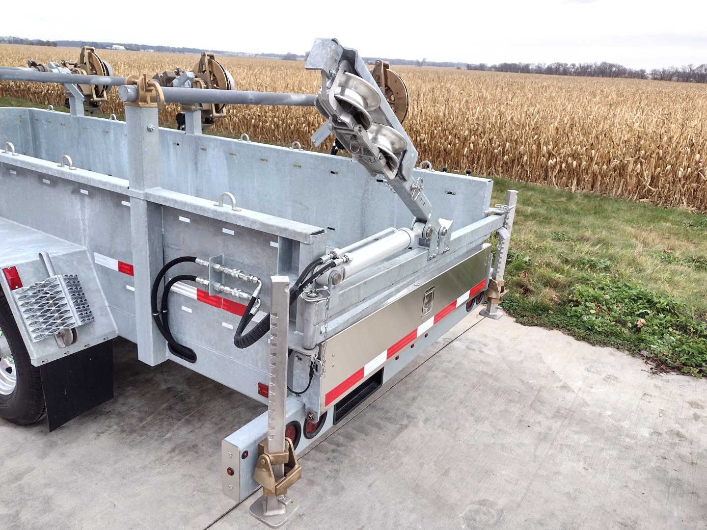 Rear tight view of level wind system mounted on a Sauber Mfg. Co. Model 1530 Three Reel Trailer. The trailer is shown in front grass strip and golden corn field.