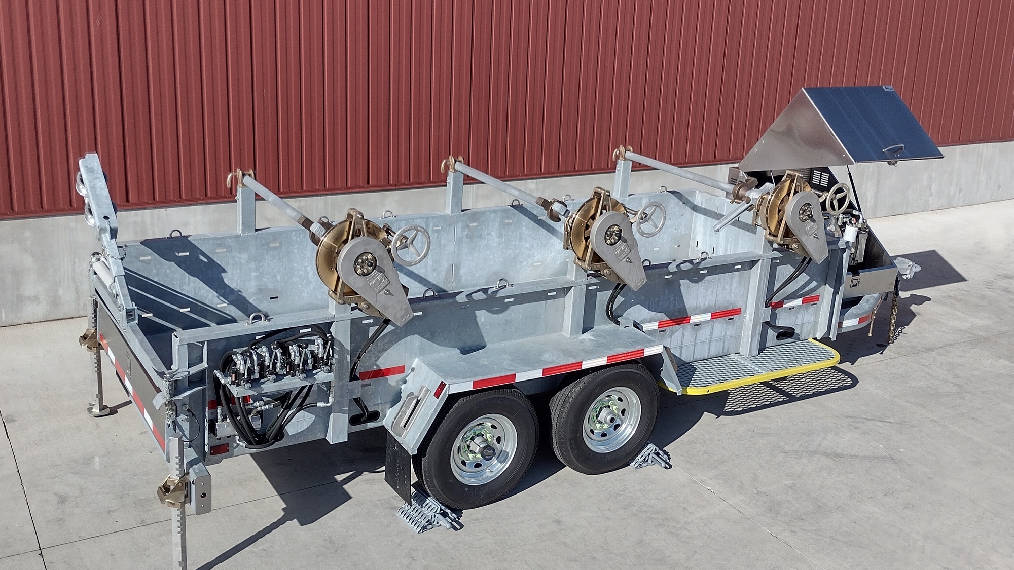 Right Rear overhead view of Model 1530 Three Reel Trailer with Model 1602 All Bronze Tensioning Brakes and Model 1000 Series Take-Up Retrievers powered by onboard Model 1010-K Power Source. The trailer is shown in front of a red metal building on concrete.