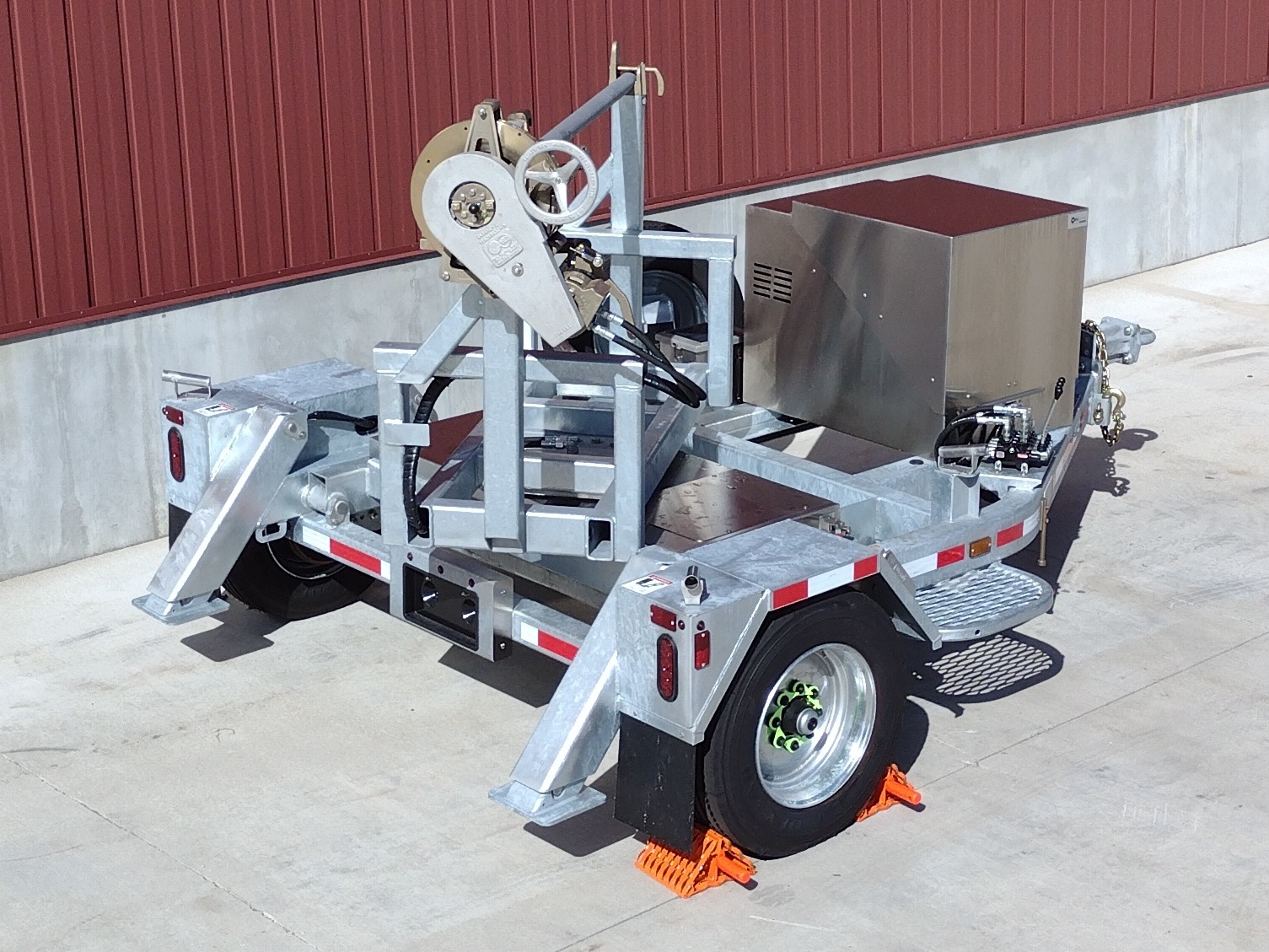 Right rear view of a Sauber Mfg. Co. Model 1519-SL Self-Loading Turret Trailer partially rotated for conductor payout. The trailer is shown on concrete in front of a red metal building.