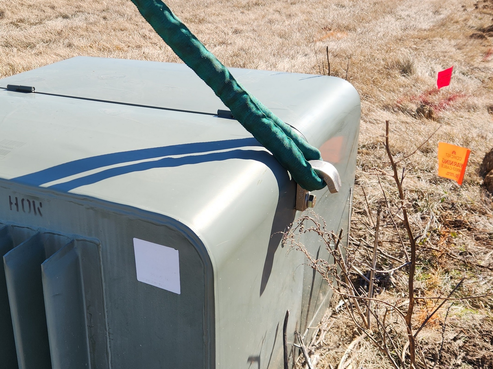 Image of Sauber Mfg. Co. Model 8051 Transformer Lifting Hook installed on green underground transformer with lifting strap. Shown at a construction area with brown vegitation.