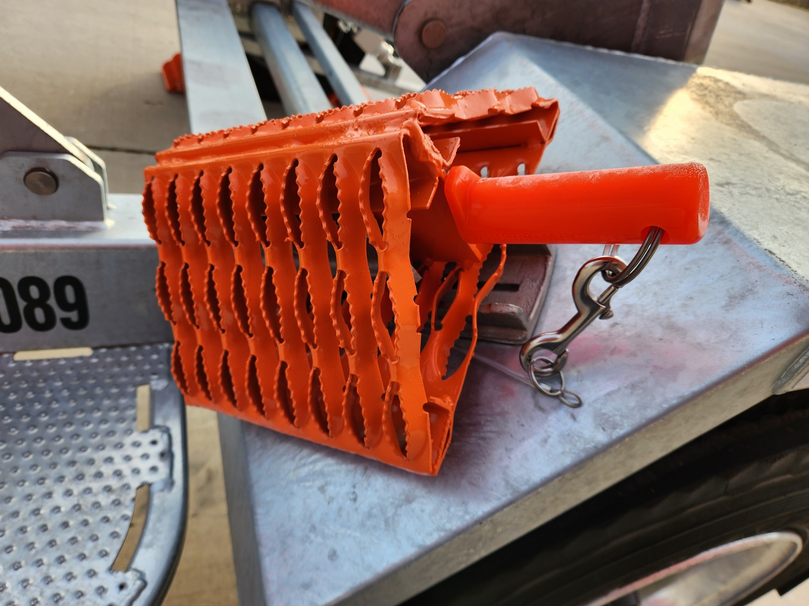 Sauber Mfg. Co. Model 8500-FO All Weather Wheel Chock with Orange Powder Coat Finish and 8501-R Almag Wheel Chock Holder mounted to trailer fender at an angle for easier access from the side.