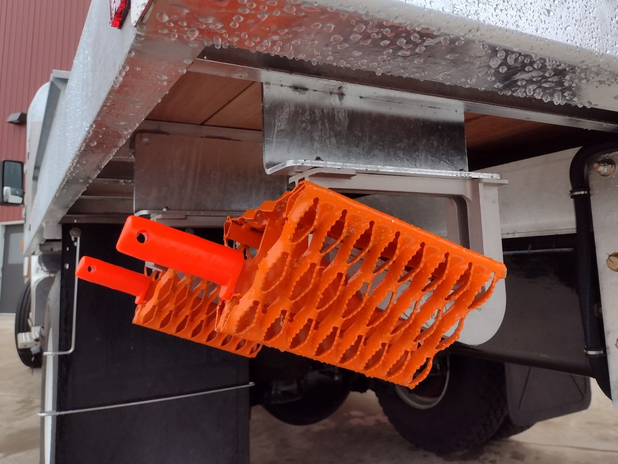 View of the underbody of a Sauber Mfg. Co. Galvanized Platform Body with Model 8500-FO All Weather Wheel Chocks in powder coat orange finish over galvanizing secured in the Model 8505-B Almag Underbody Wheel Chock Holder.