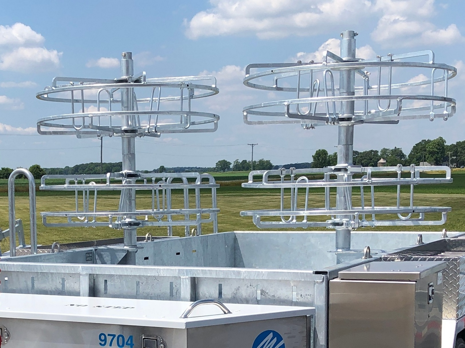 Image front right of a Sauber Mfg. Co. Dual Hand Coil Reel with galvanized finish. Shown mounted to a trailer in front of a field and blue sky.