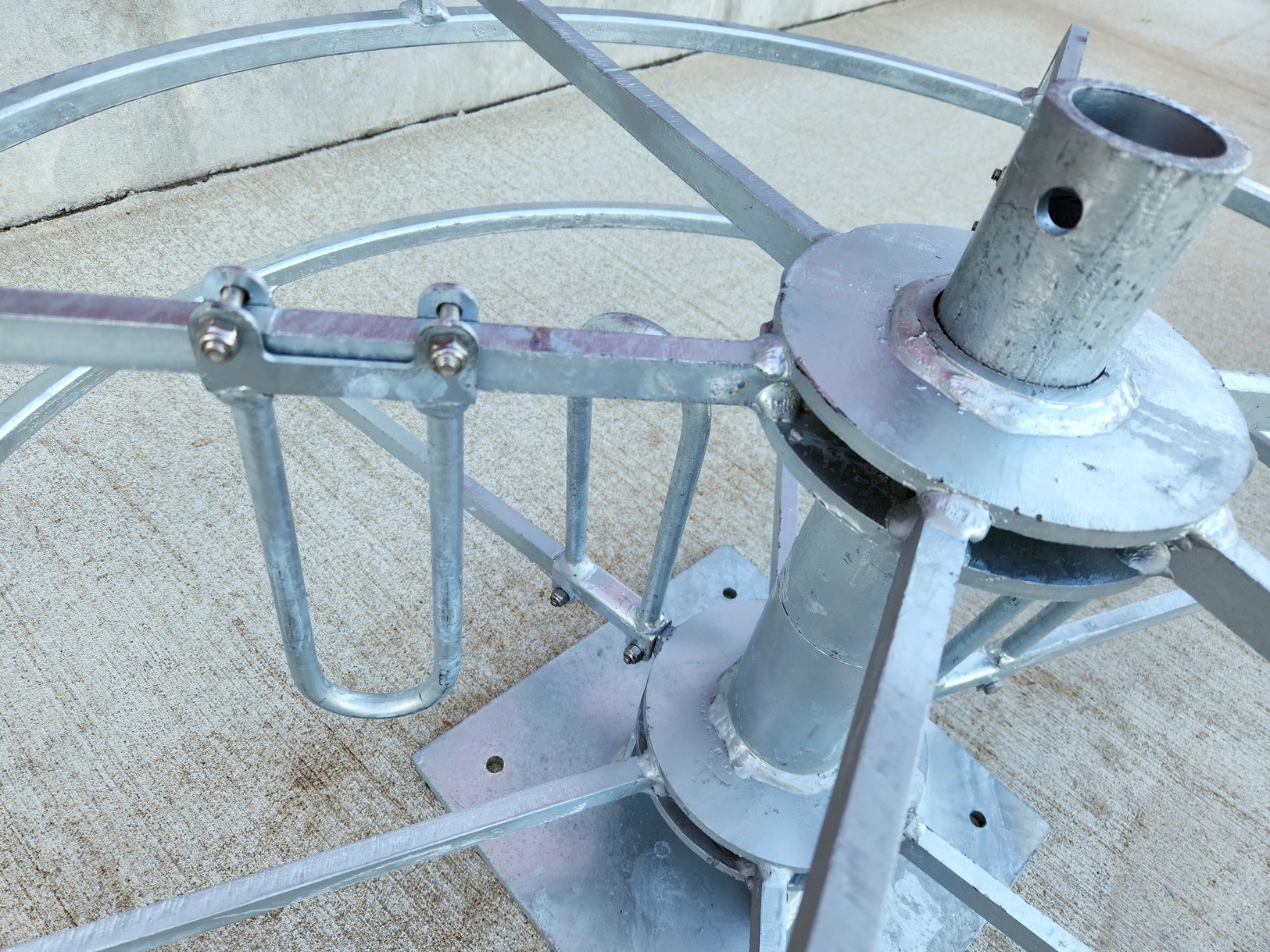 Close image from above at three-quarter angle of a Sauber Mfg. Co. Hand Coil Reel adjustable inner diameter loop. The hand coil reel has hot dipped galvanized finish. The part is shown on Concrete with concrete building foundation in the background.