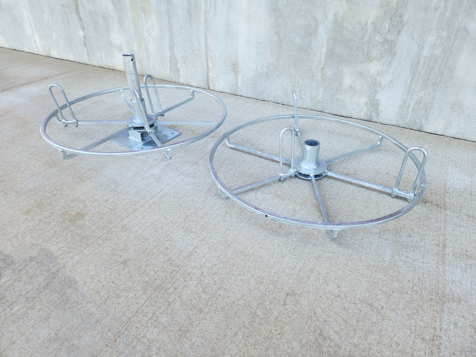 Image from above at three-quarter angle of a Sauber Mfg. Co. Hand Coil Reel with galvanized finish. The top clam shell reel flange is removed to show how a coil is loaded into the reel. The parts are shown on Concrete with concrete building foundation in the background.