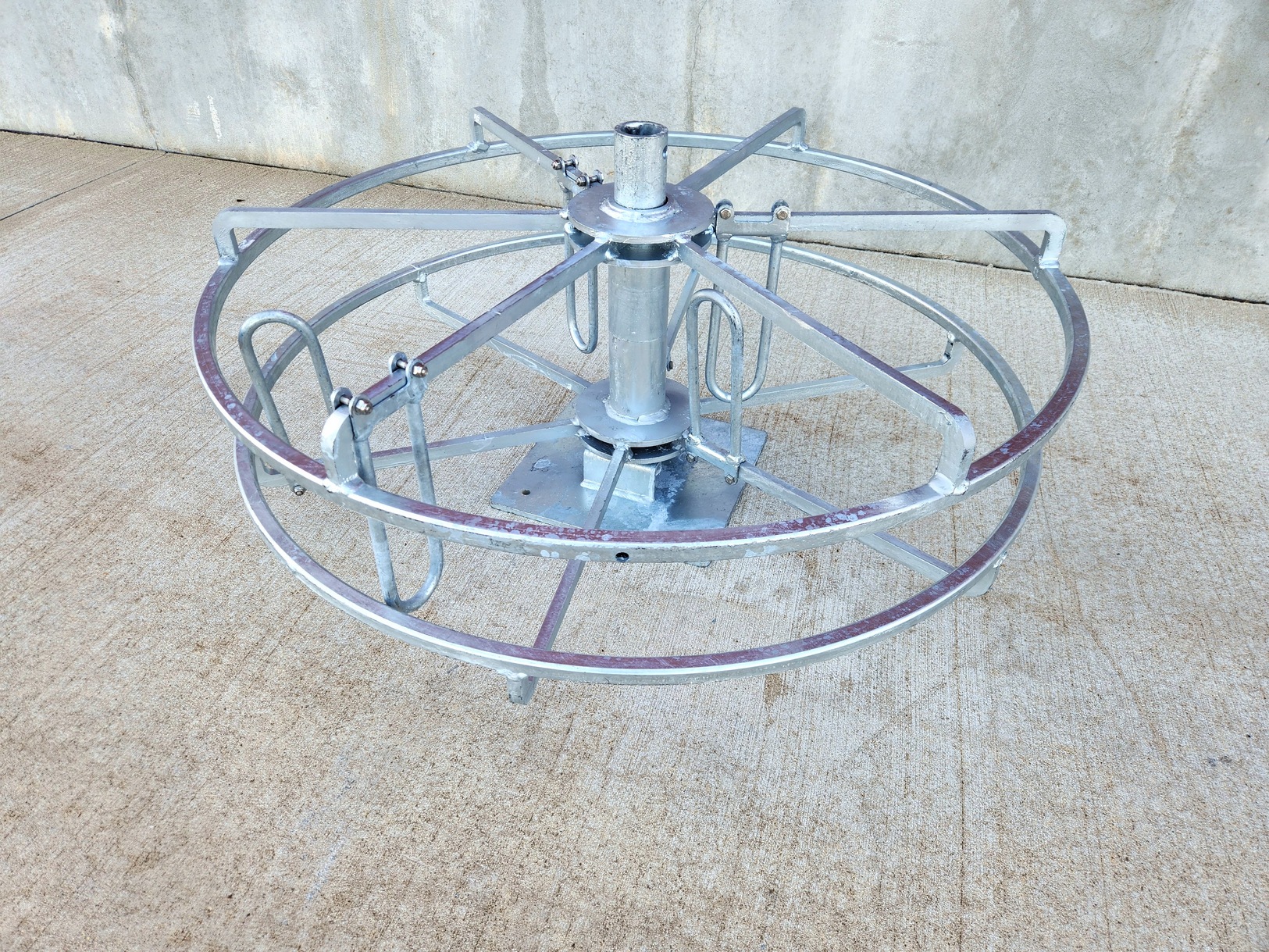 Image from above at three-quarter angle of a Sauber Mfg. Co. Hand Coil Reel with galvanized finish. Shown on Concrete with concrete building foundation in the background.