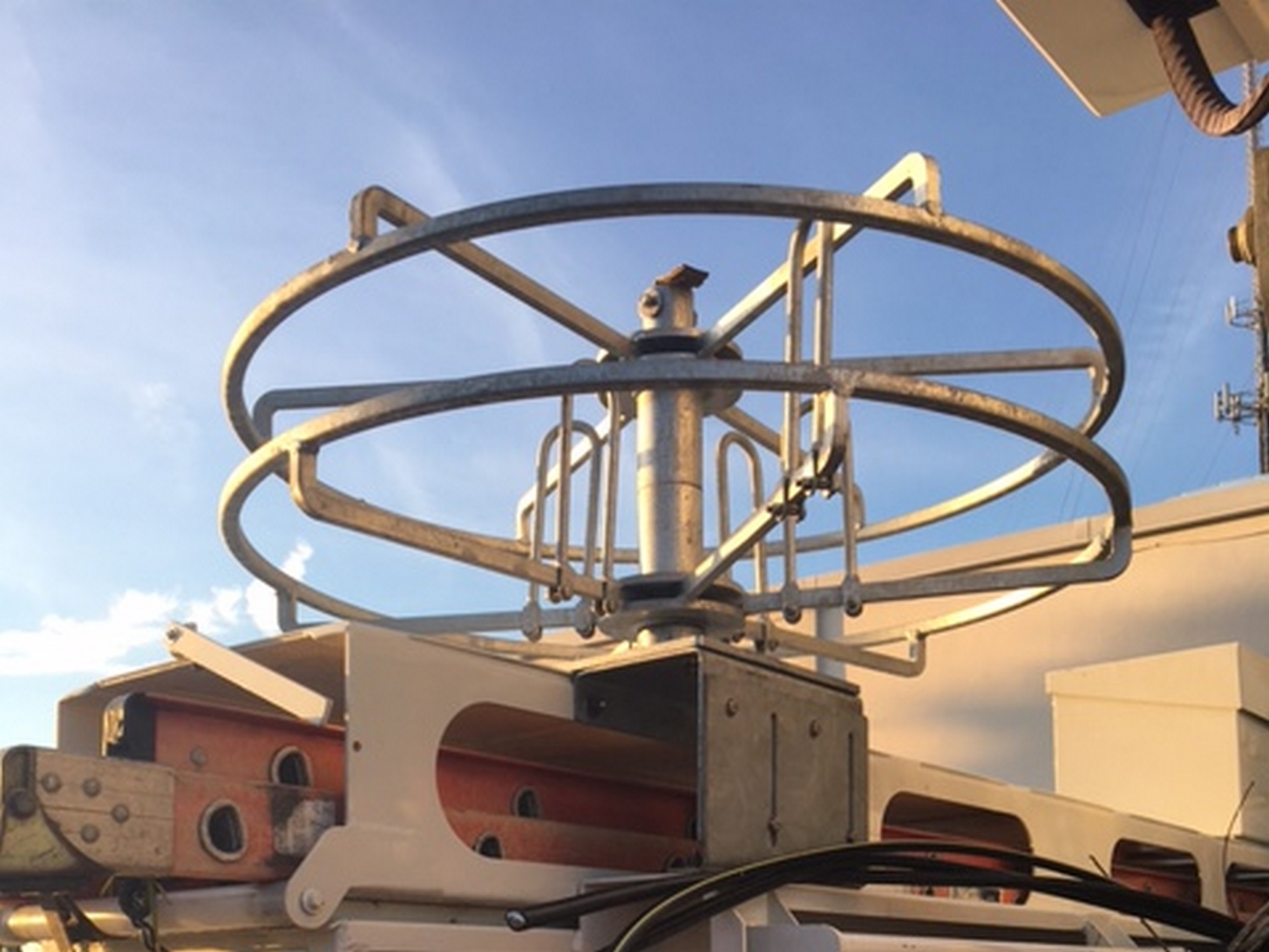 Rear image from below of a compartment top mounted Sauber Mfg. Co. Hand Coil Reel with adjustable inner diameter and hot dipped galvanized finish. The available adjustable mounting bracket kit is also shown. There is blue sky in the background.