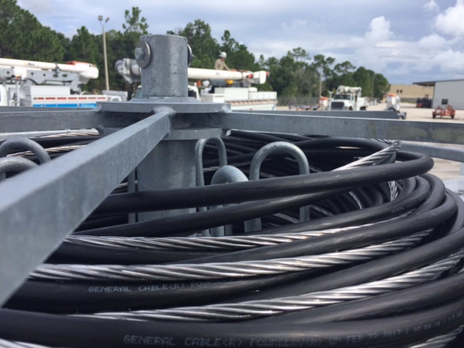 Image of the top clamshell flange of a Sauber Mfg. Co. Hand Coil Reel with galvanized finish loaded with a tri-plex hand coil. There is equipment and a blue sky in the background.