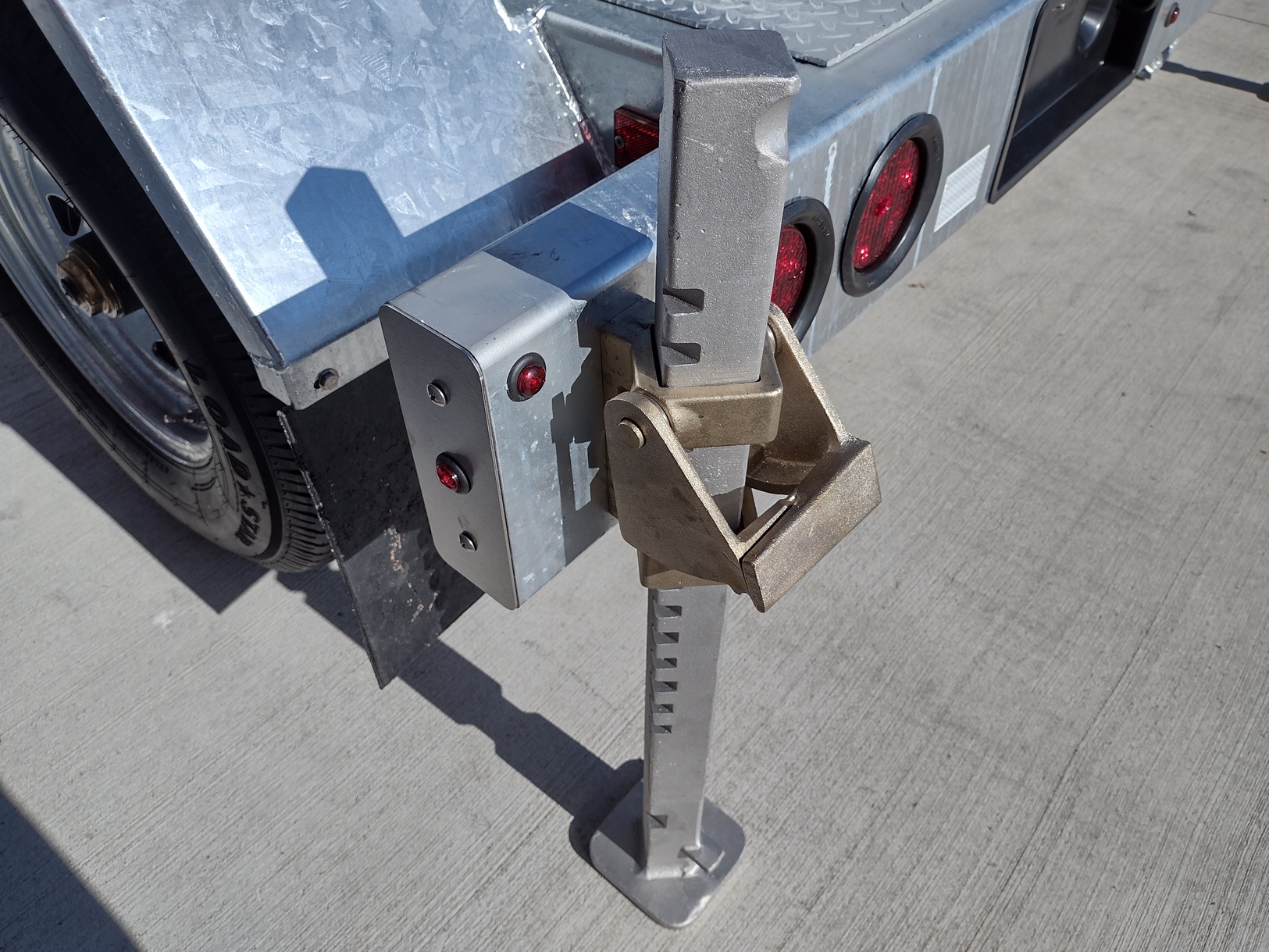 Daytime close view from above of a Sauber Mfg. Co. Trailer with Model 8805 Almag Outrigger Jack in the deployed position. The trailer is shown on concrete in full sunshine.