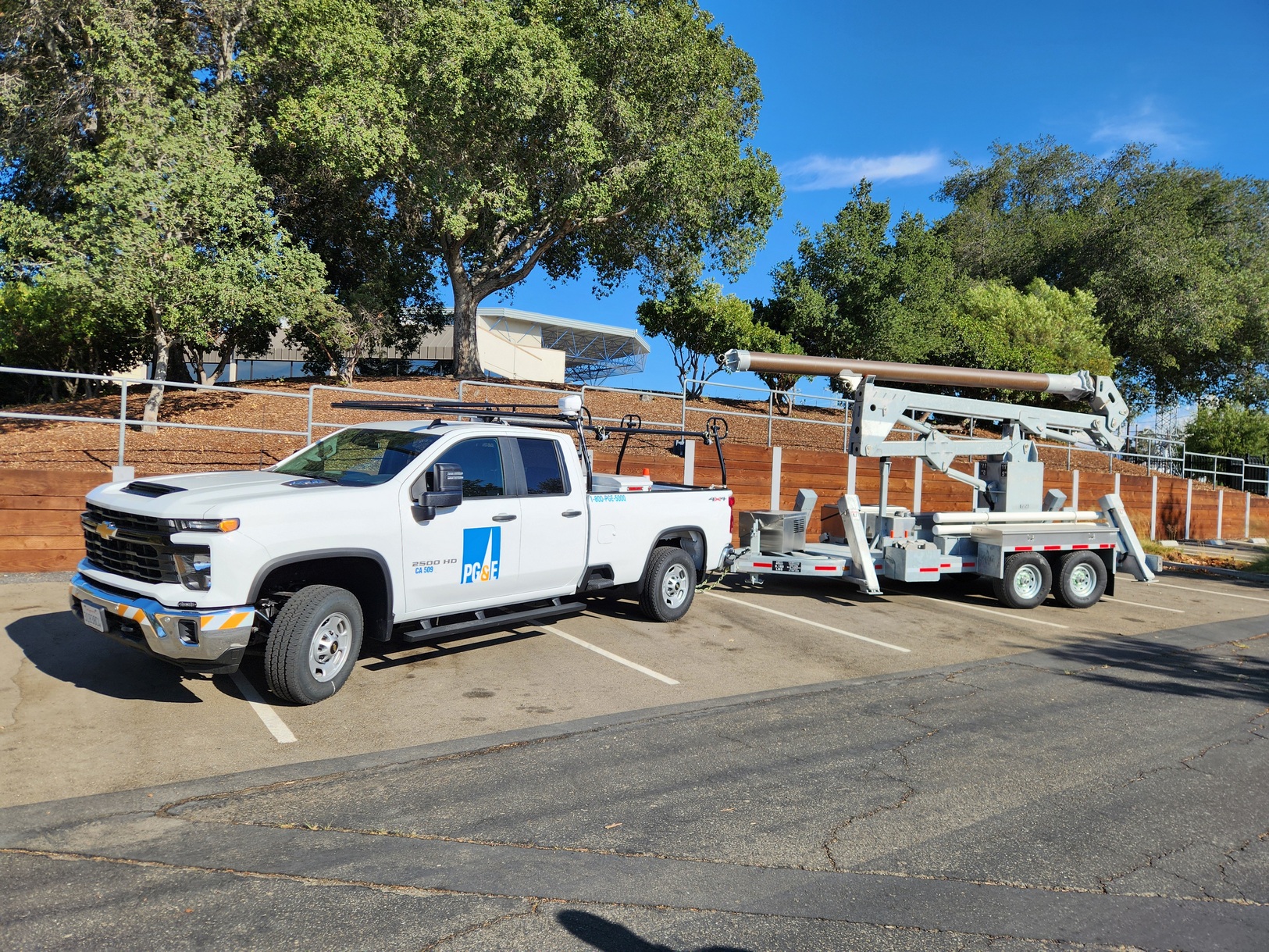 Right side view from front of a Model 1572 Rapid Overhead Deployment Trailer in tow behind a 3/4 Ton Supervisor's truck. There are trees and mulch in the background on a sunny day with blue skies.